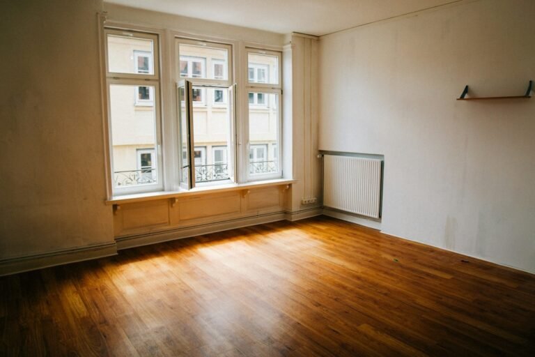 An empty, minimalist room with a wooden floor and large window